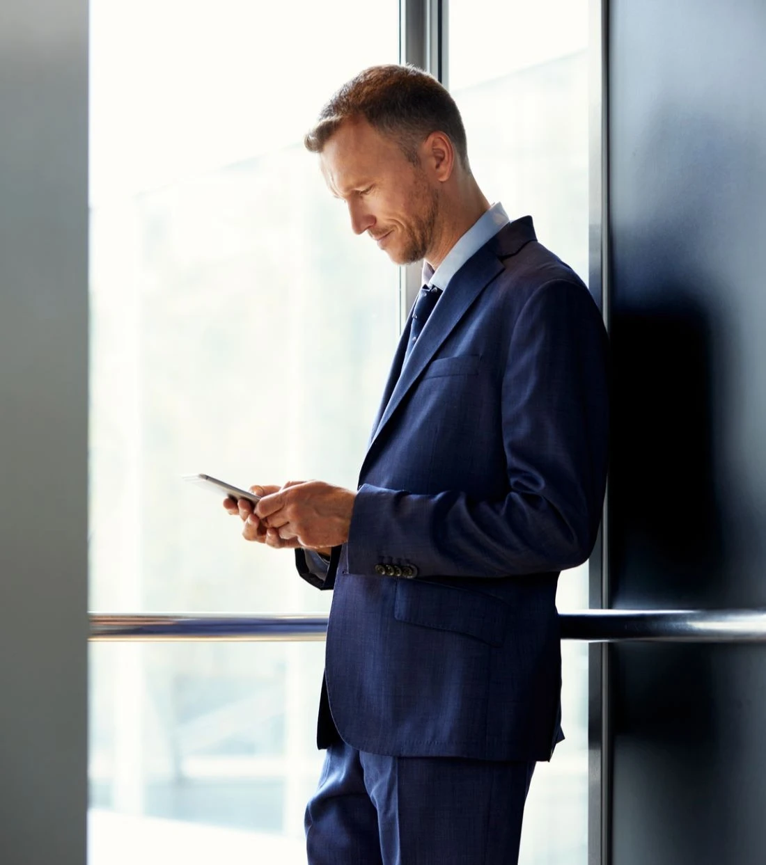 A man who leans against the wall is looking at the phone