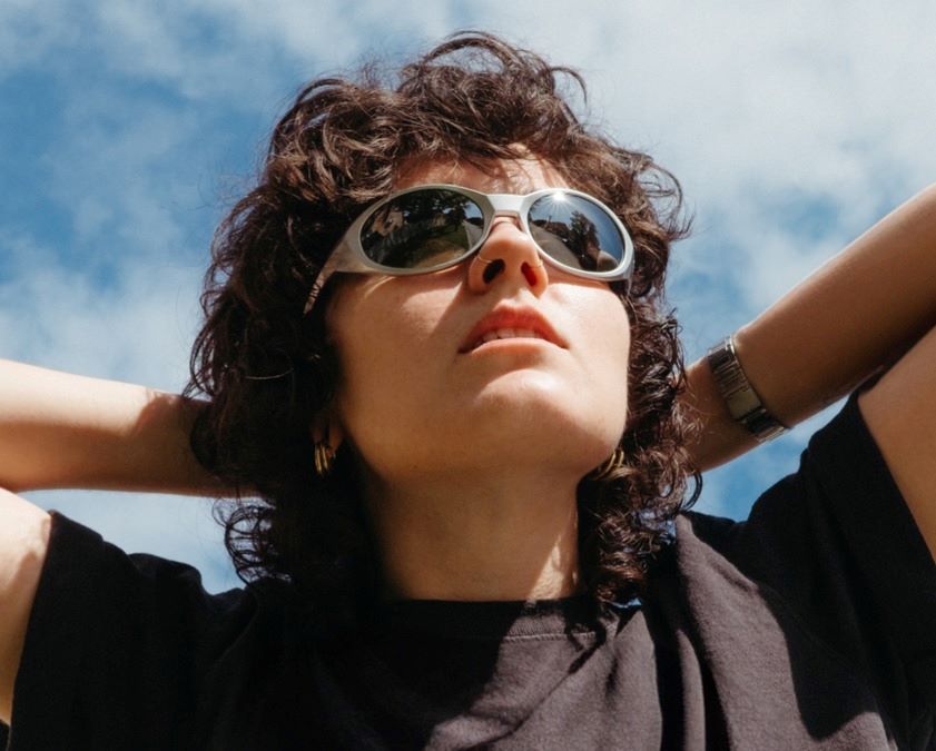 A girl with curly black hair and sunglasses holding her hands on the head
