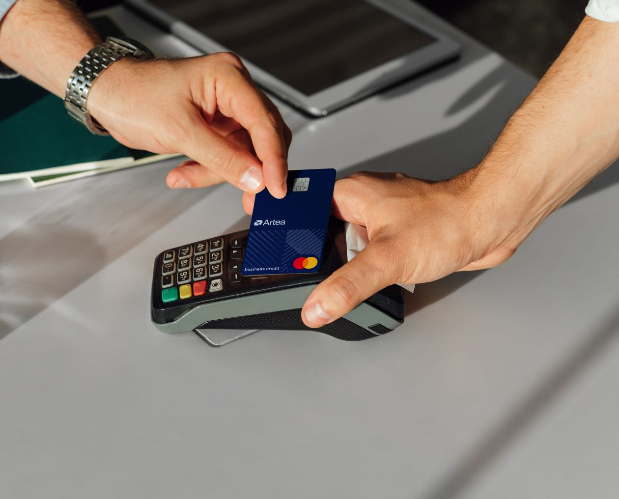 One hand places the Mastercard Business card next to the card reader, while the other hand holds the reader