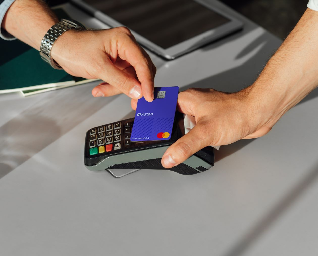 One hand places the Mastercard Business card next to the card reader, while the other hand holds the reader