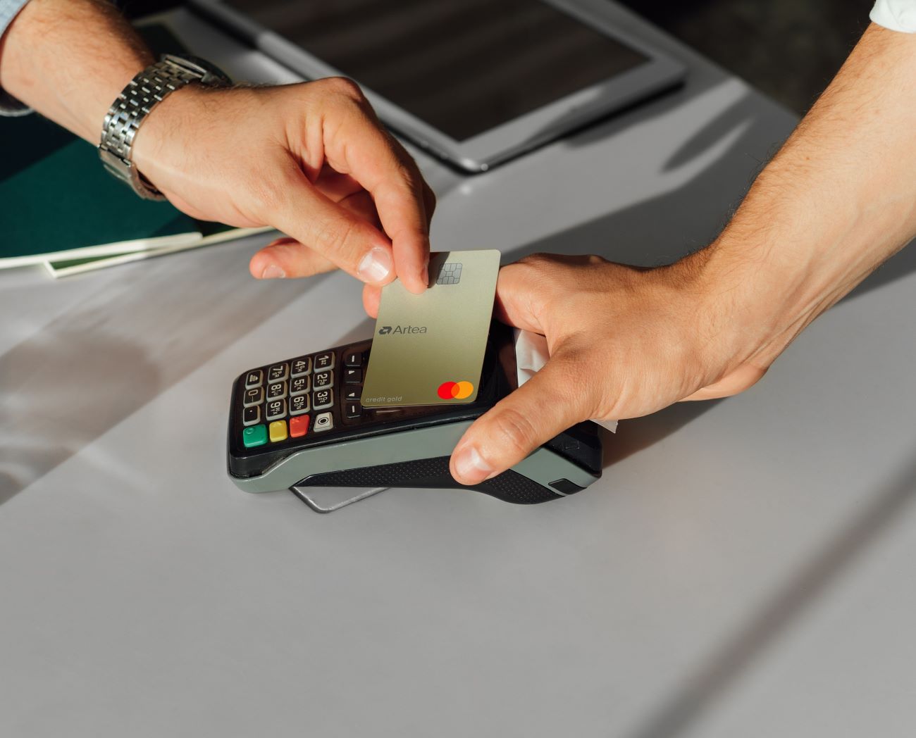 Ranka deda Mastercard Gold kortelę prie kortelių skaitytuvo, kita ranka laiko skaitytuvą